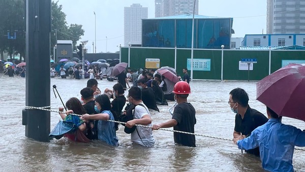 역대급 폭우가 내린 중국 허난성 정저우시에서 수많은 시민들이 20일 도로를 가르지도록 설치된 로프를 잡고 허리까지찬 물속을 걸어 안전한 곳으로 피해가고 있다. 사진=차이나데일리